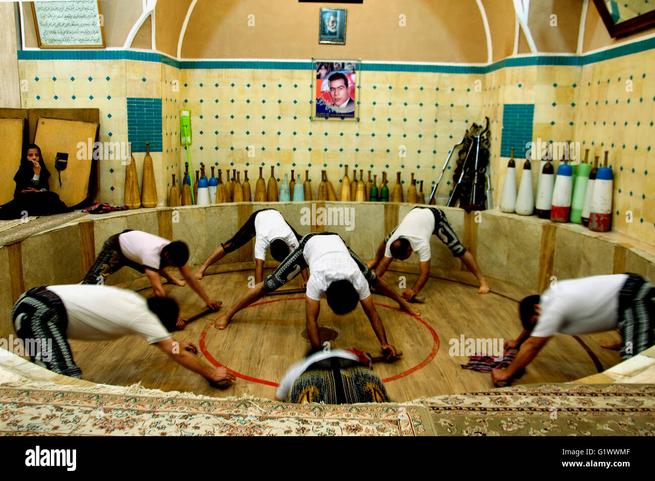 In Yazd, Iran, gli uomini e i ragazzi fare calisthenics in una tradizionale sala zurkaneh; una giovane ragazza in un chador, forse un relativo, sta guardando Foto Stock