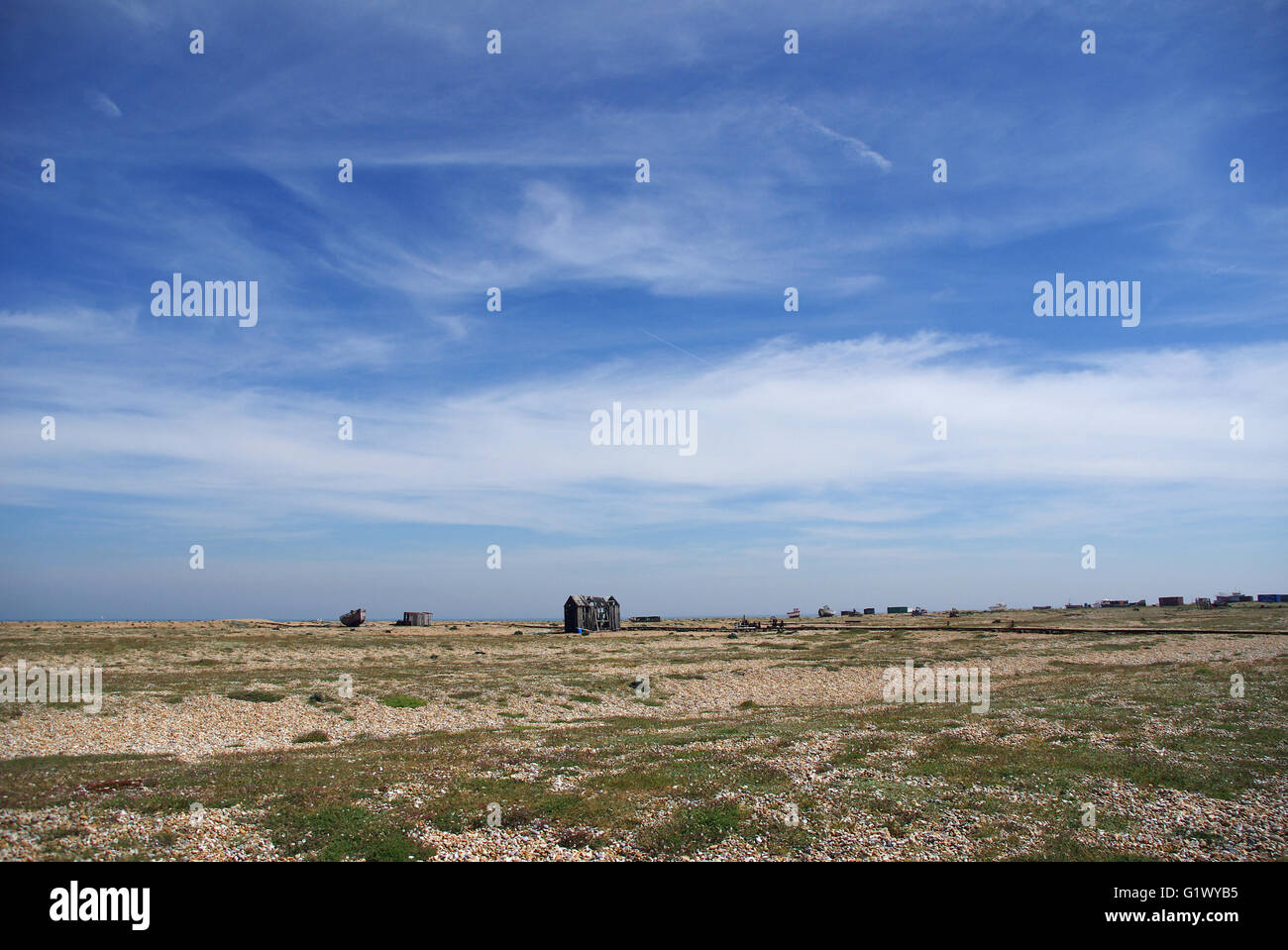 Spiaggia di Dungeness guardando giù per il canale in lingua inglese e in disuso degli edifici in rovina nella distanza con big blue sky Foto Stock