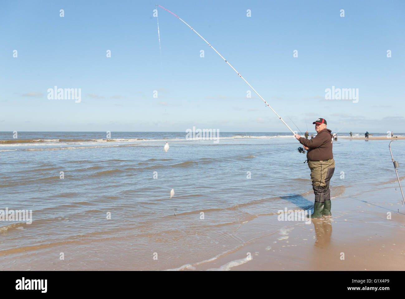 Uomo di Fisher in waders marrone con maglioni e cappuccio in possesso di una canna da pesca con due catturato il pesce. Doppia chiusura presso la spiaggia del Mare del Nord Foto Stock