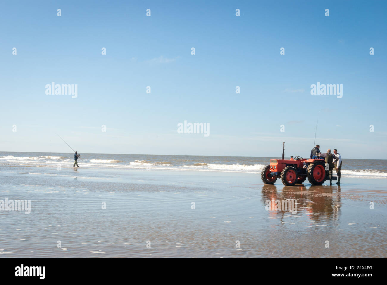 Trattore rosso con la chat pescatori sulla spiaggia del Mare del Nord e uno fisher con la canna da pesca attiva in background. Foto Stock