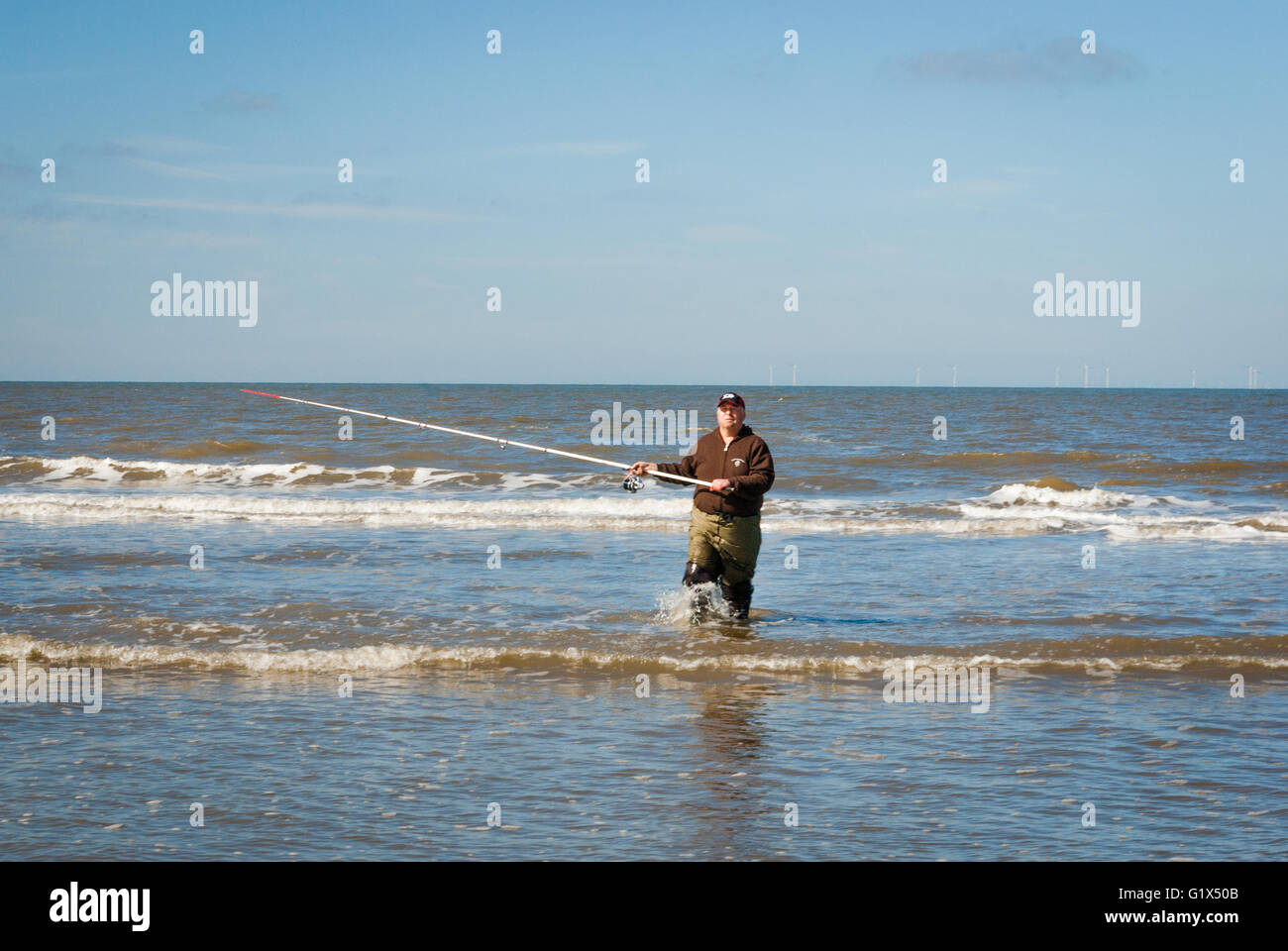 Pescatore con canna da pesca alle ginocchia in acqua wading torna dal mare a riva dopo la fusione la linea Foto Stock