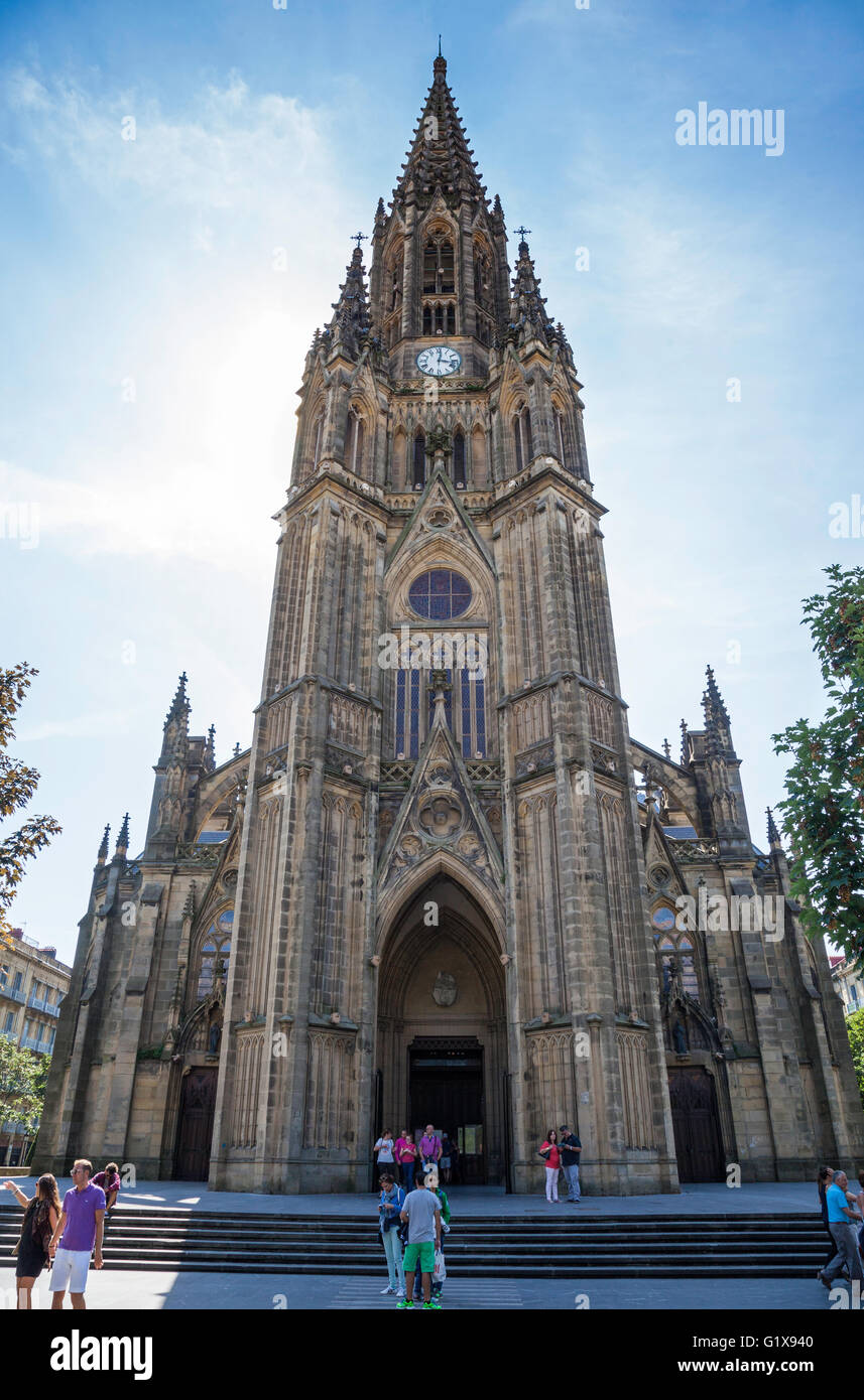 Facciata ornata della torre di orologio della Cattedrale di Buen Pastor, San Sebastian, Spagna contro un cielo blu e turisti in primo piano Foto Stock