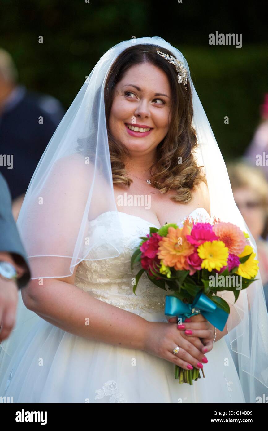 Sposa sorridente holding fiori durante il suo giorno di nozze indossando abiti da sposa Foto Stock