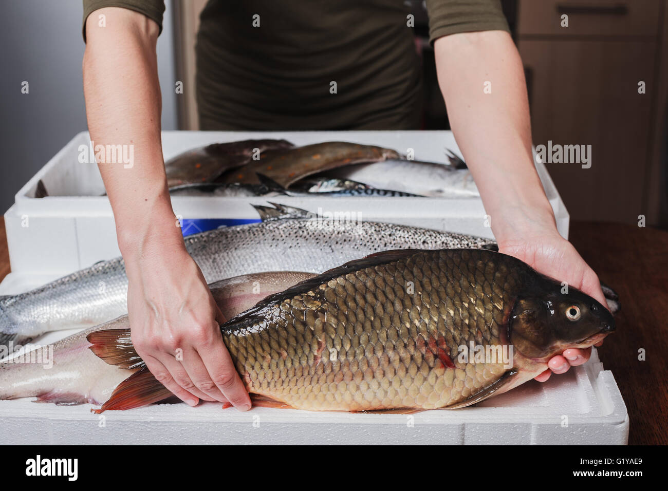 Una giovane donna di smistamento è una scatola di pesce fresco a casa nella sua cucina Foto Stock