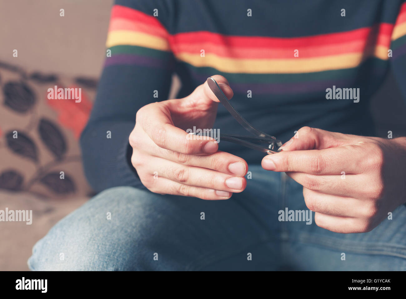 Un giovane uomo è seduto su un divano e clipping è il suo dito unghie Foto Stock