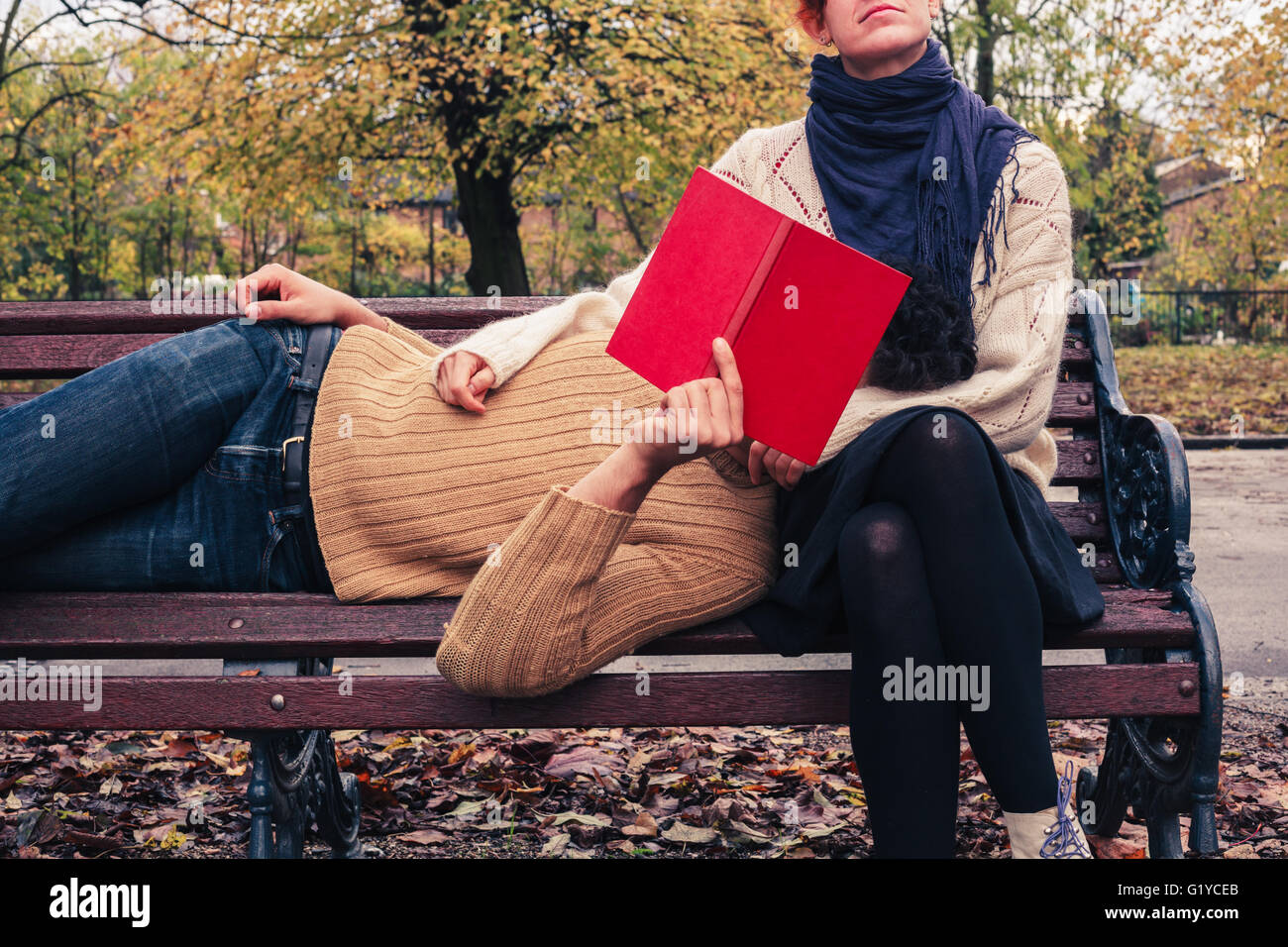 Una giovane coppia è la lettura e il relax su una panchina nel parco in autunno Foto Stock