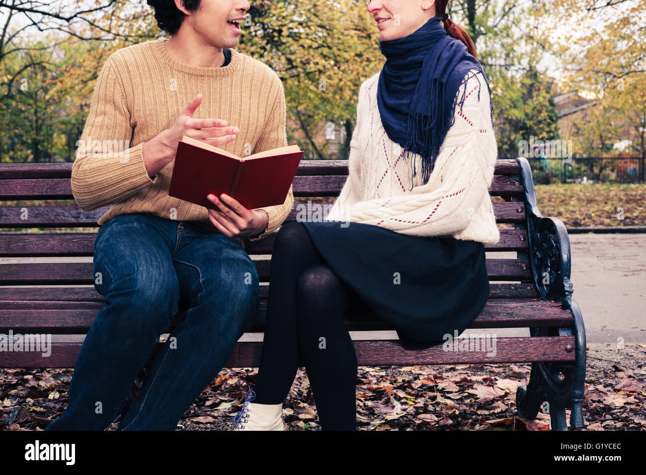 Un giovane uomo è la lettura di una giovane donna su una panchina nel parco in autunno Foto Stock
