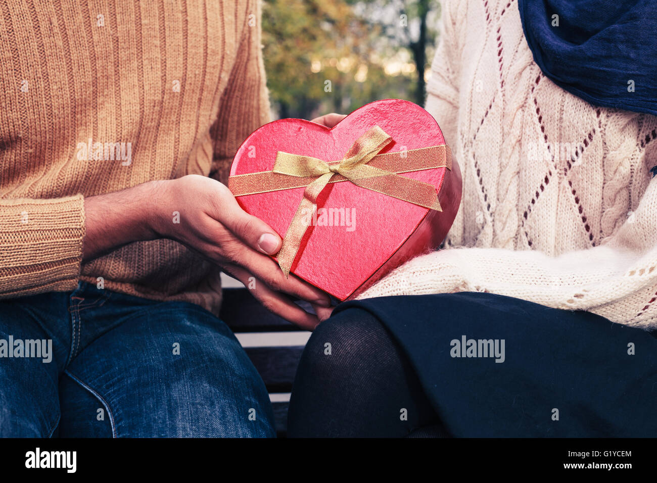 Un giovane uomo è dare una donna un cuore scatola sagomata nel parco Foto Stock