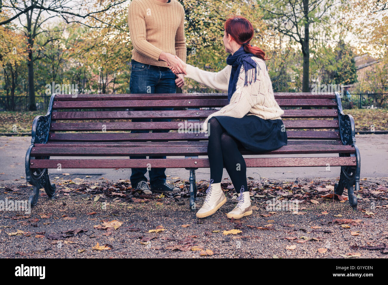 Una giovane donna seduta su una panchina del parco è di incontrare un uomo nel parco e sono le mani di scuotimento Foto Stock