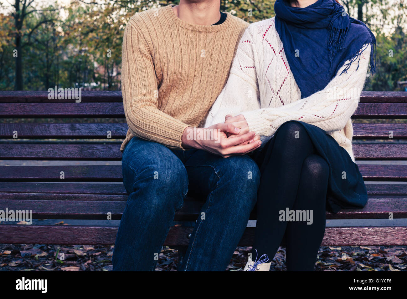 Un youg giovane è seduta e la tenuta di ciascun altro su una panchina nel parco in autunno Foto Stock