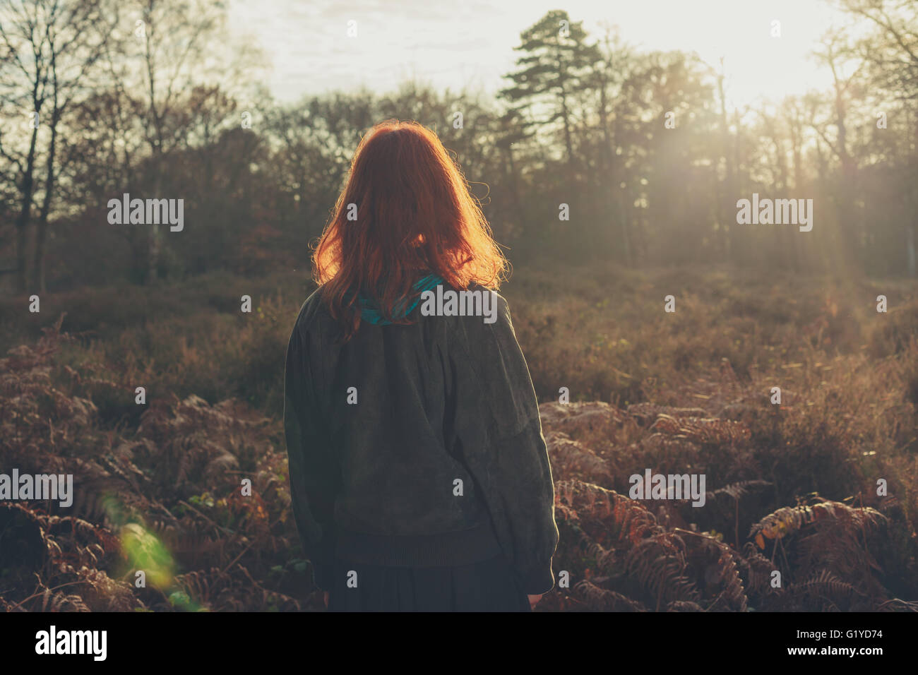 Una giovane donna è in piedi in una foresta al tramonto Foto Stock