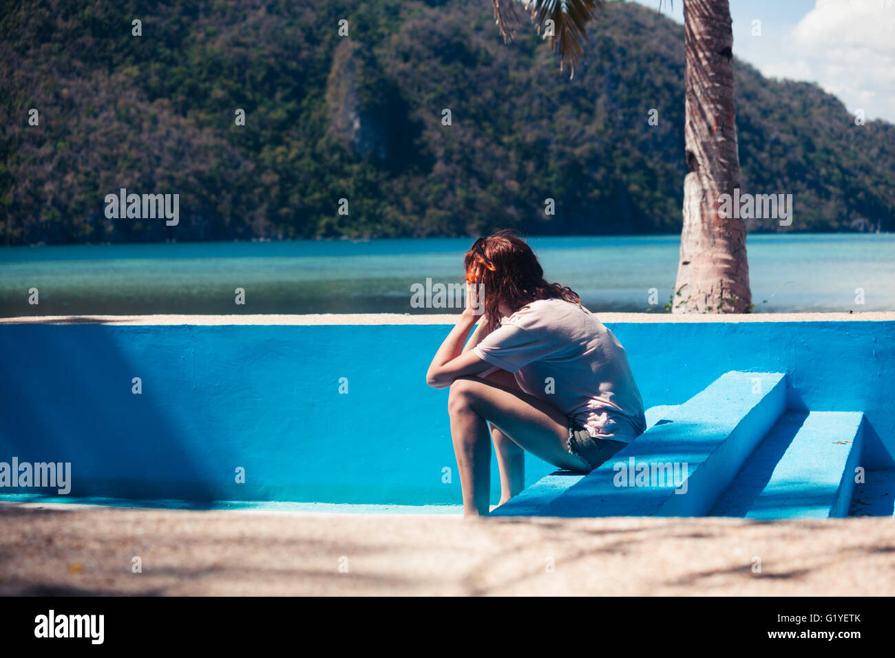 Un triste giovane donna con il suo capo nelle sue mani è seduto in un vuoto di piscina in spiaggia Foto Stock