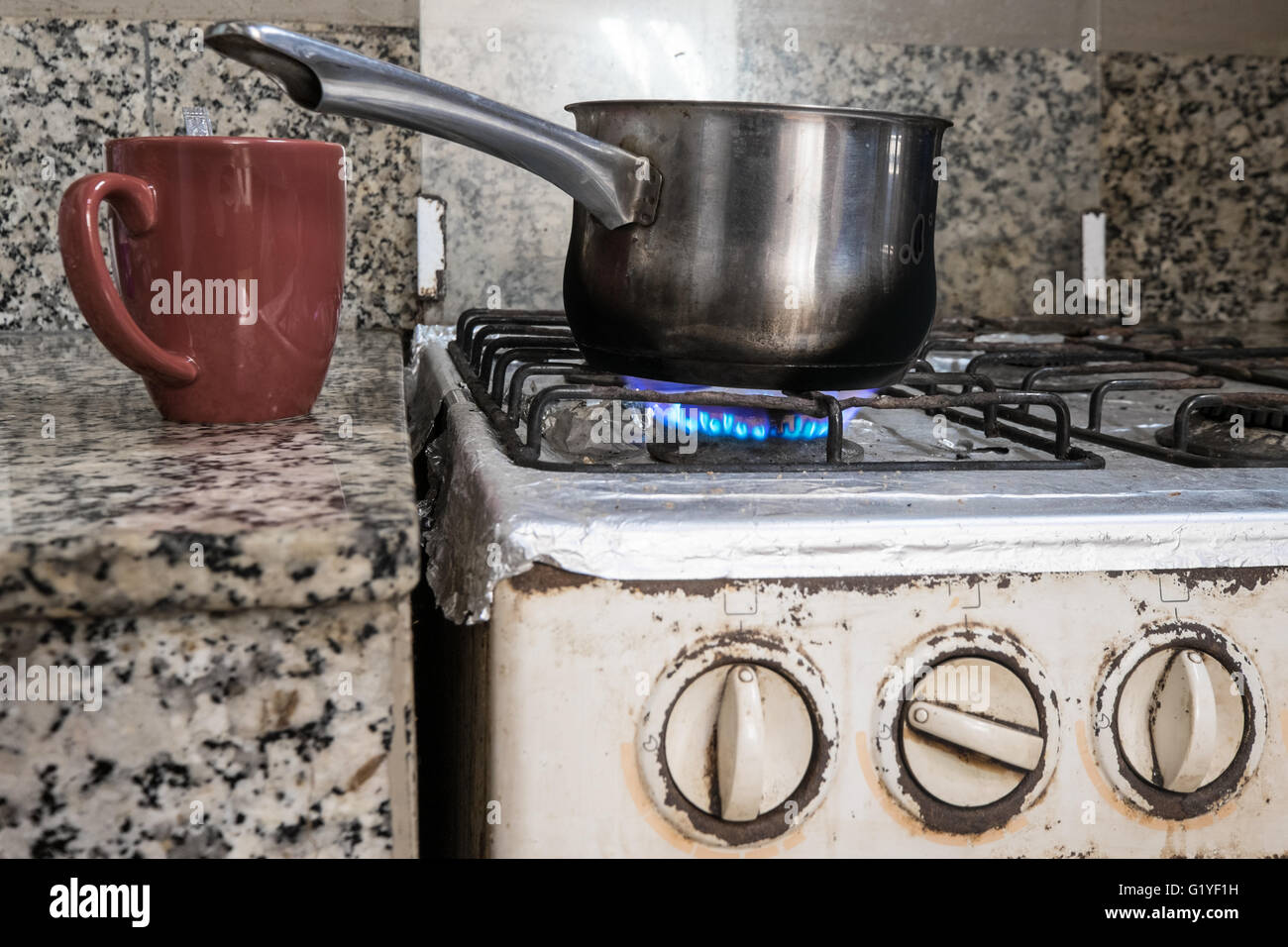 Una sola tazza accanto a una pentola di acqua su un vecchio fornello a gas / fornello Foto Stock
