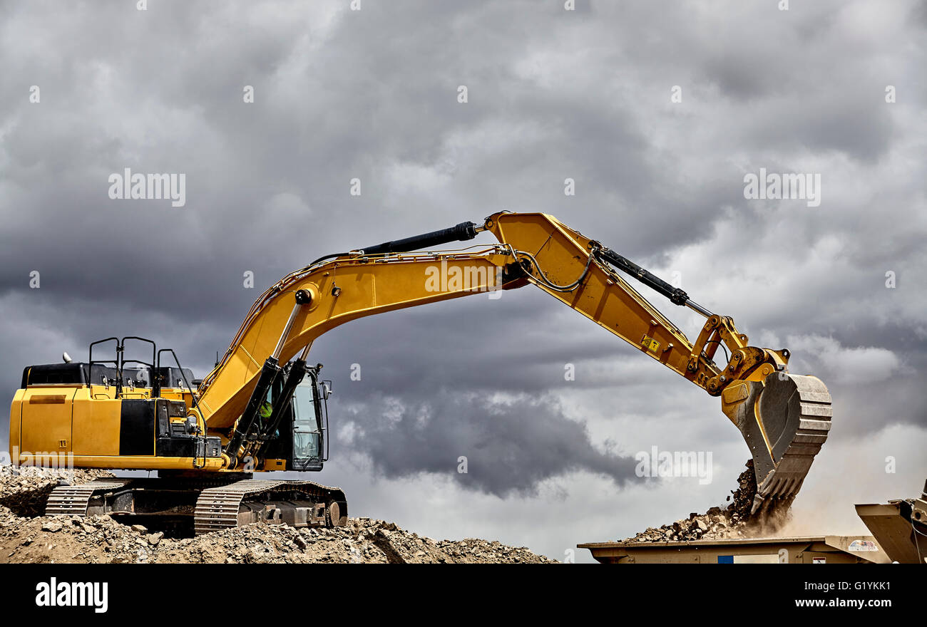Industria di costruzione di apparecchiature pesanti escavatore ghiaia di movimentazione in cantiere cava con cielo tempestoso Foto Stock