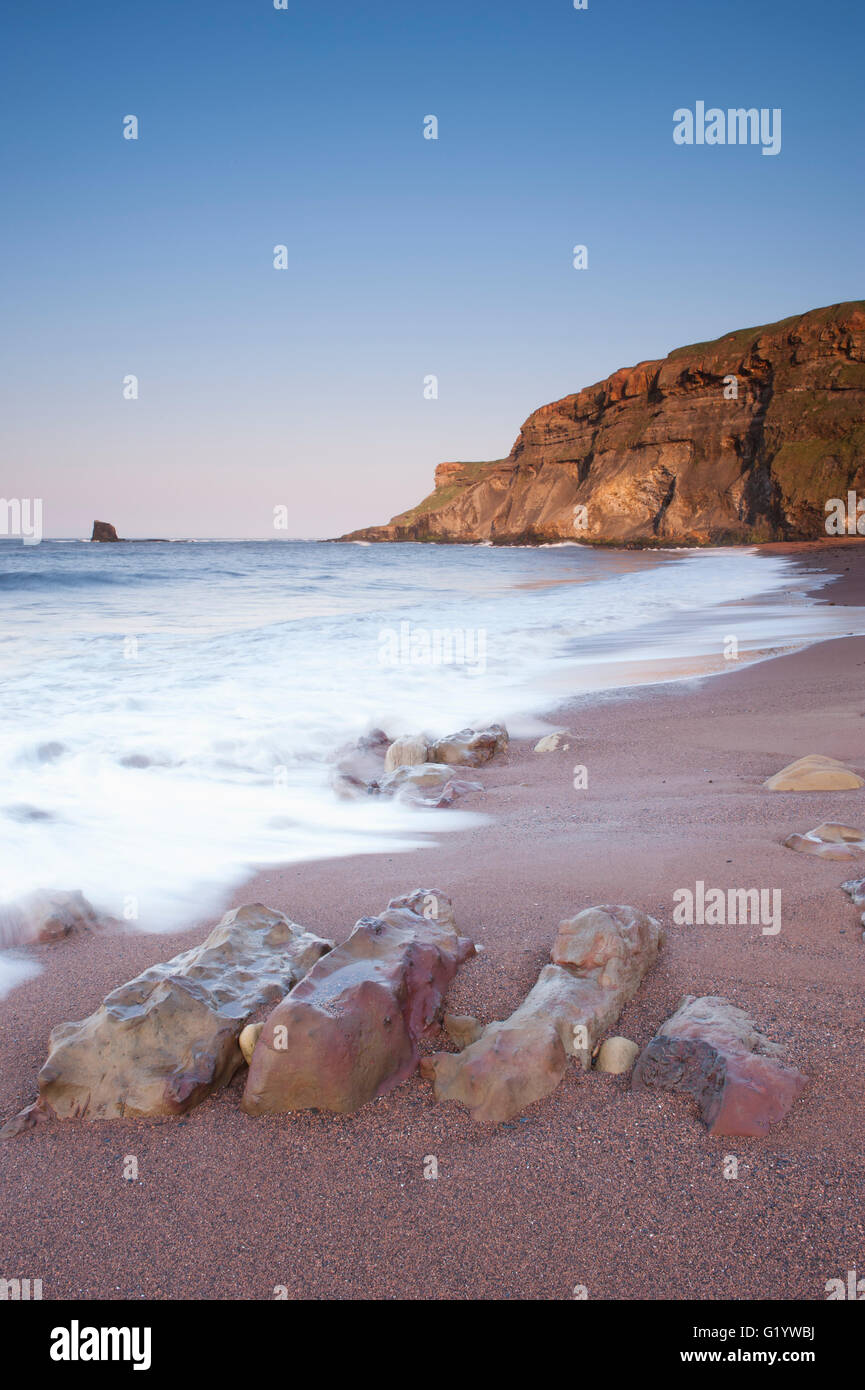 Torreggianti scogliere, Nero Nab, mare calmo, liscia sabbia, spiaggia rocciosa, cielo azzurro e sole serale - pittoresche Saltwick Bay, North Yorkshire, GB, UK. Foto Stock
