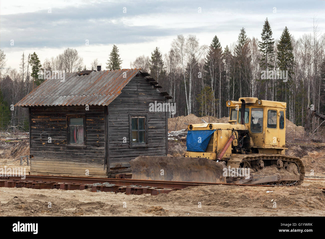 Bulldozer giallo nella sabbia vicino alla casa in legno in una foresta Foto Stock