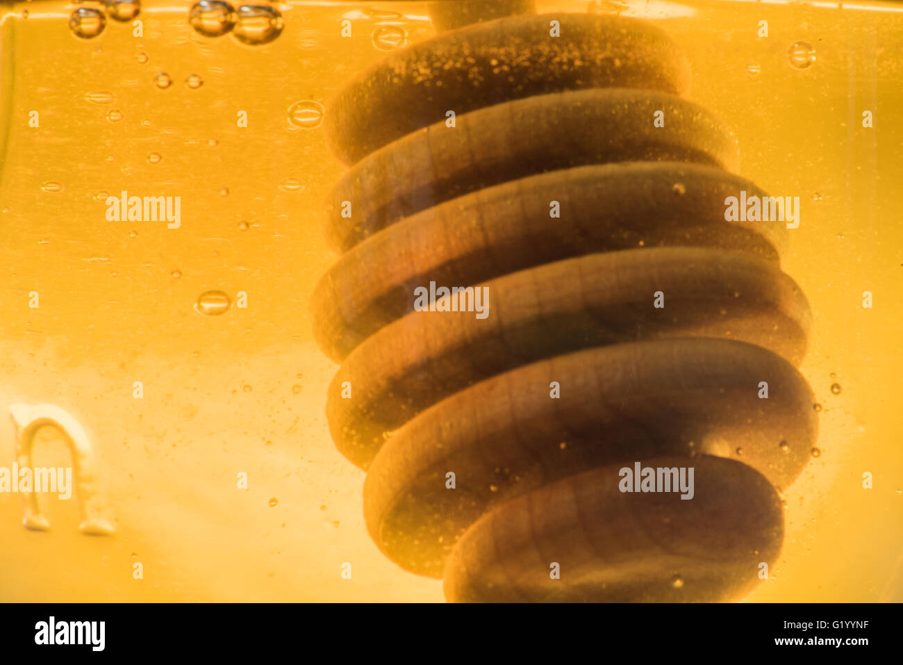 Il miele in legno bilanciere in un barattolo di vetro di miele con bolle di aria Foto Stock