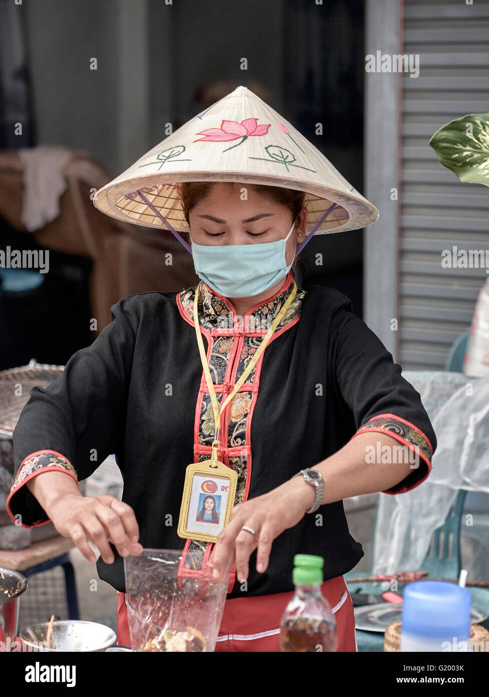 Thailandia fornitore di cibo di strada indossando una mascherina igienica mentre prepara il cibo in un mercato cinese di strada. S. E. Asia. Foto Stock