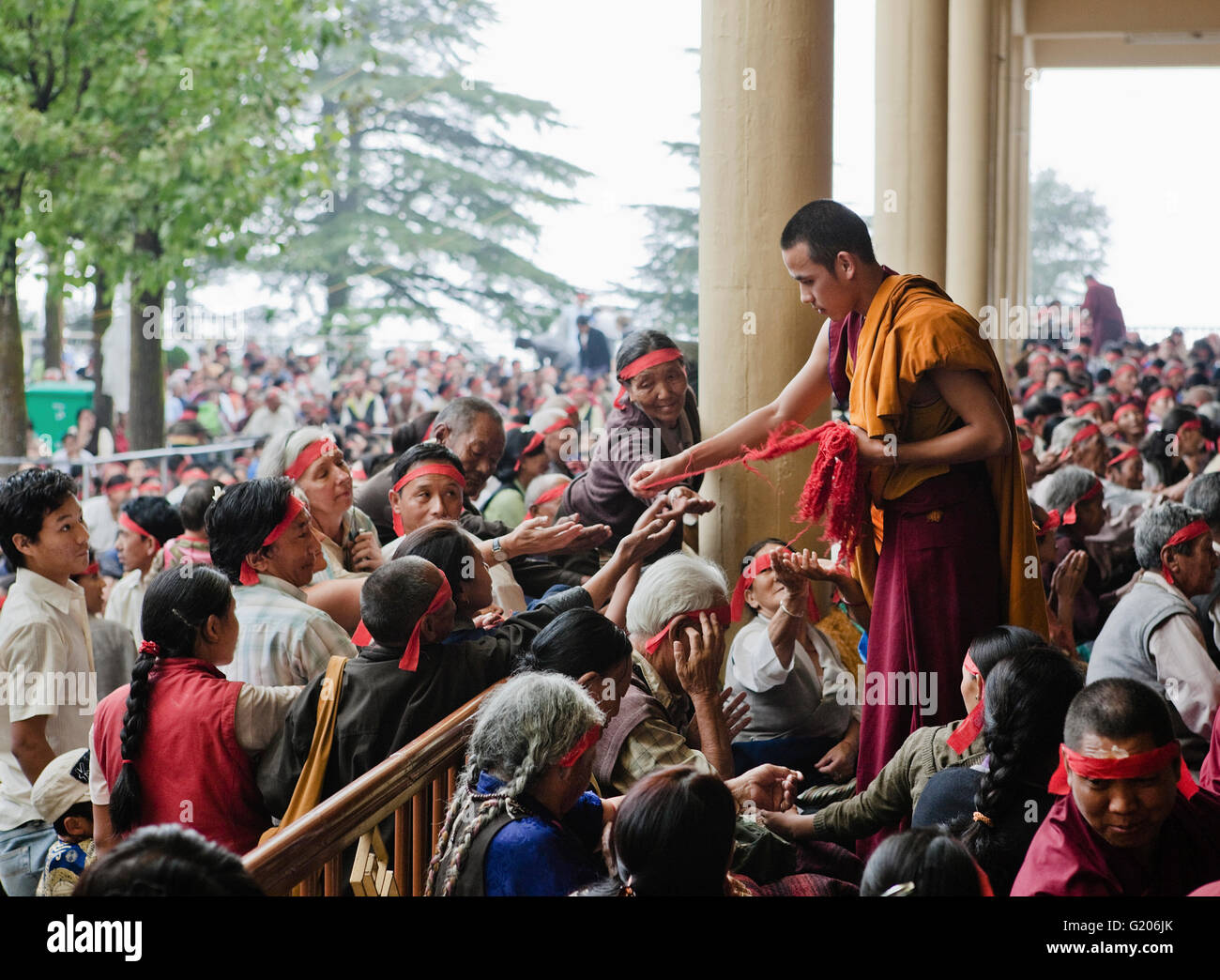 Un monaco tibetano distribuisce panno rosso prima di bande di Chenrezig iniziazione mediante il Dalai Lama al tempio Tsuglagkhang. India Foto Stock