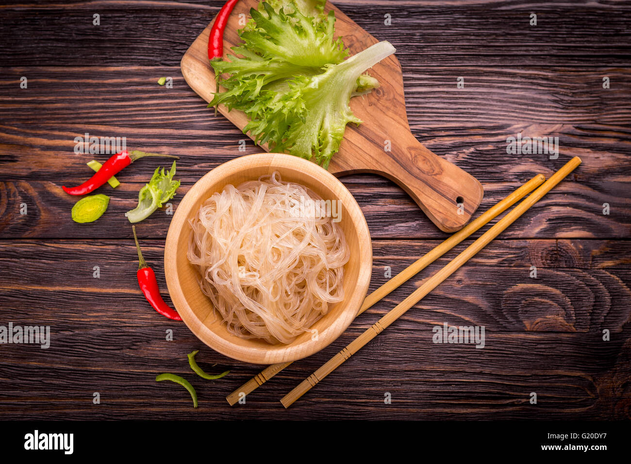 Ingredienti della cucina asiatica - Riso tagliatelle, porro, lattuga, red hot pepper al buio su un sfondo di legno Foto Stock