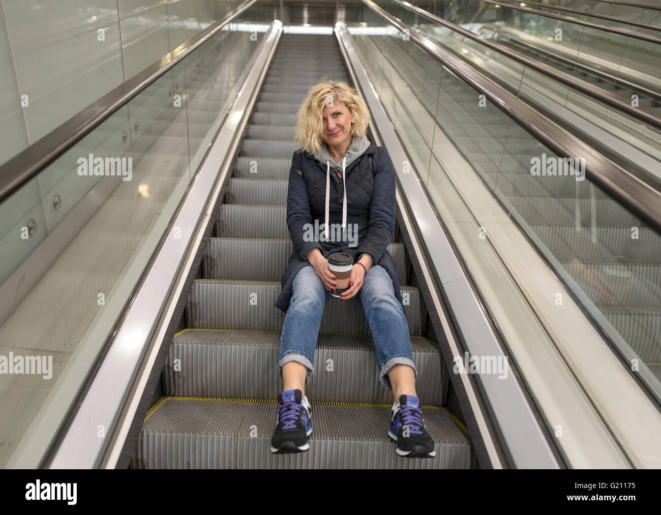 Blondie ragazza è di posti a sedere su per le scale di escalator Foto Stock