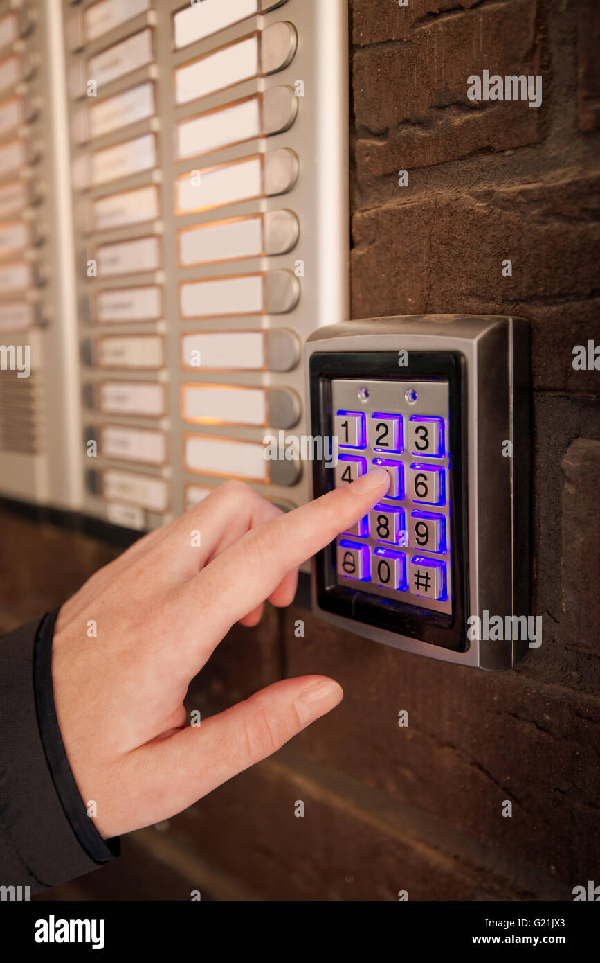 Donna di comporre il codice di accesso sulla tastiera di sicurezza intercom per aprire la porta di ingresso del palazzo di appartamenti. Foto Stock