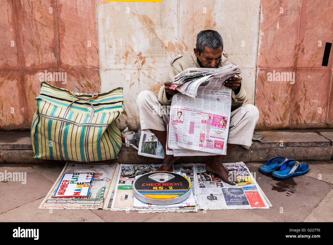 Uomo di carta di lettura mentre egli attende i clienti a pesare stessi, Delhi, India Foto Stock