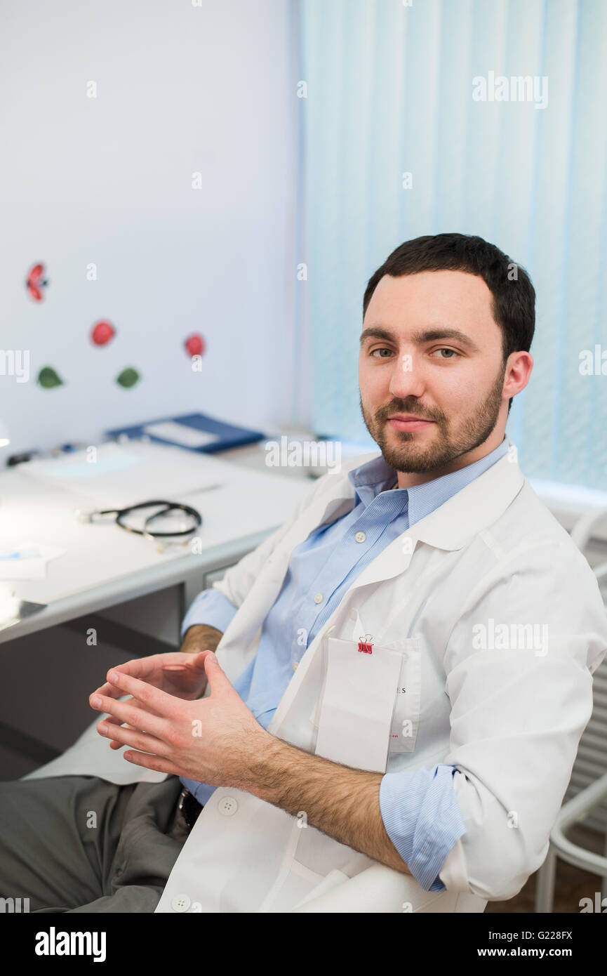 Calma medico o consulente seduto alla scrivania con il suo stetoscopio sul tavolo cercando per la fotocamera Foto Stock