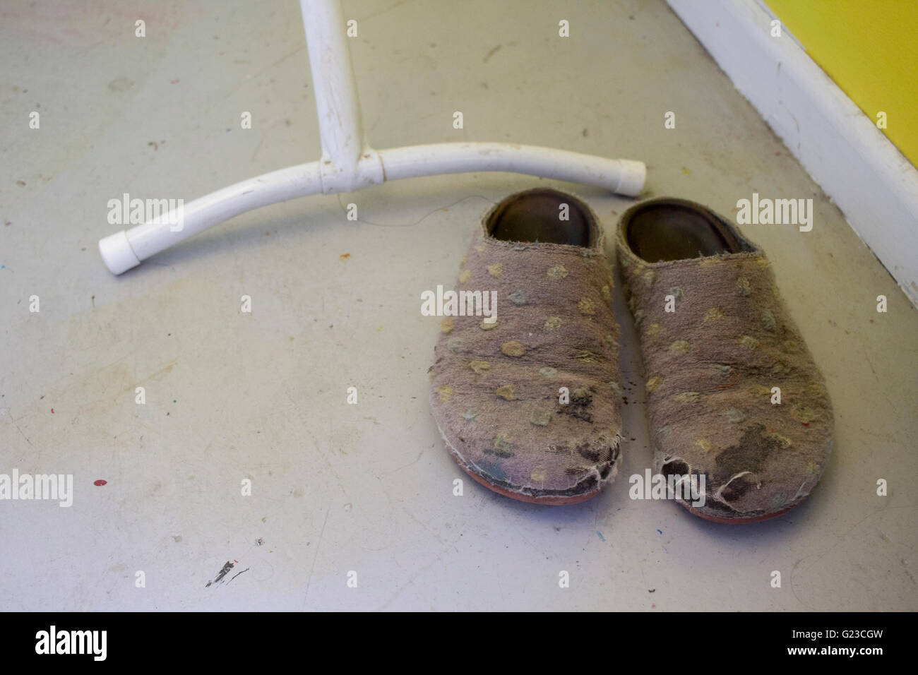 Coppia di ben indossati pantofole accanto ai piedi di un asse da stiro, Foto Stock
