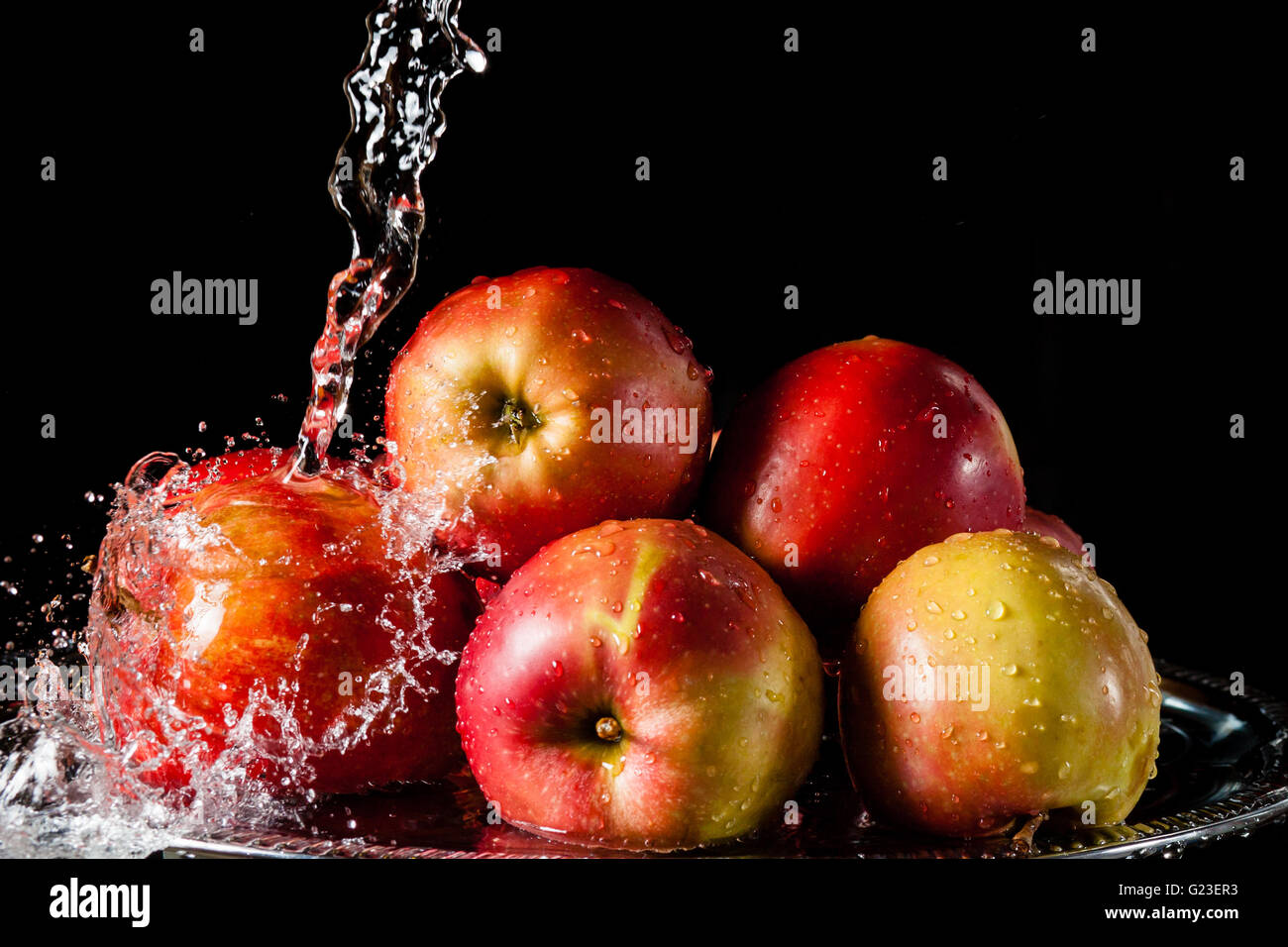 Poche le mele rosse giacente su un silver top e caduta di acqua su sfondo nero Foto Stock