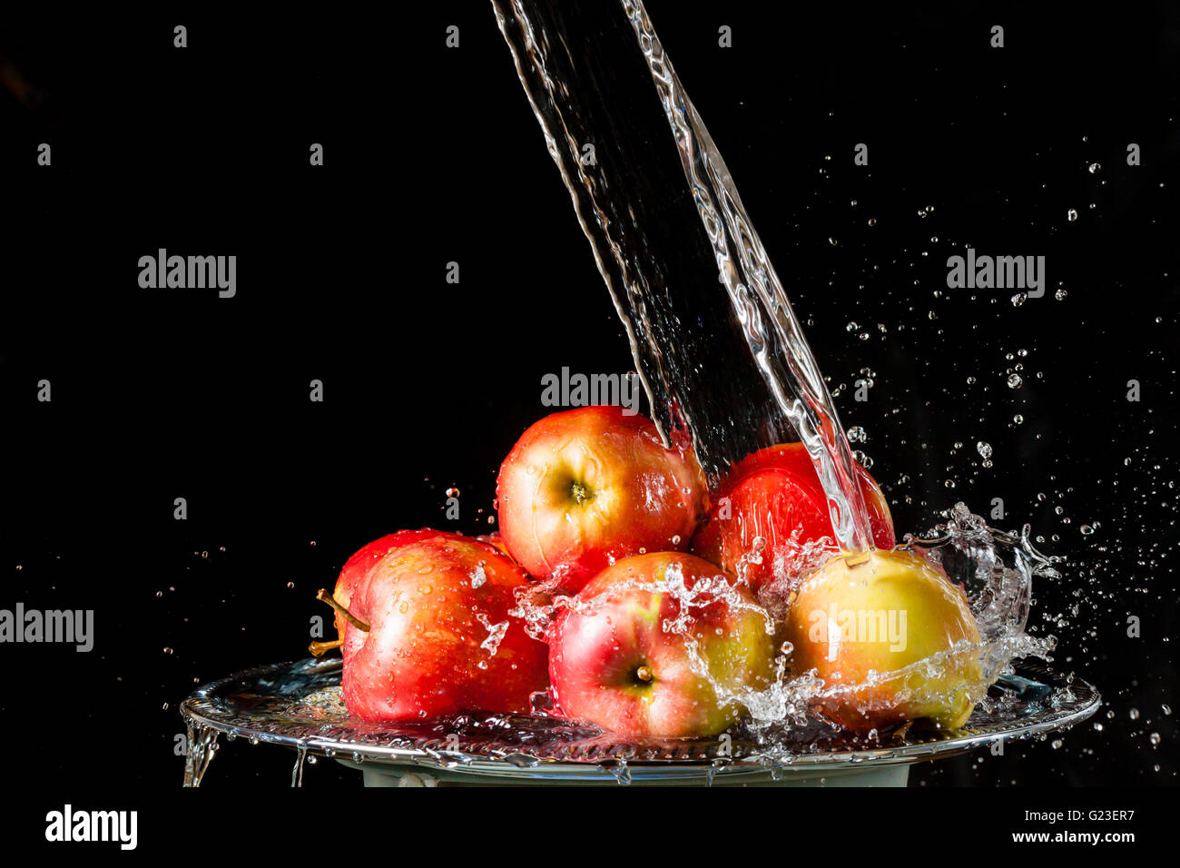 Poche le mele rosse giacente su un silver top e caduta di acqua su sfondo nero Foto Stock