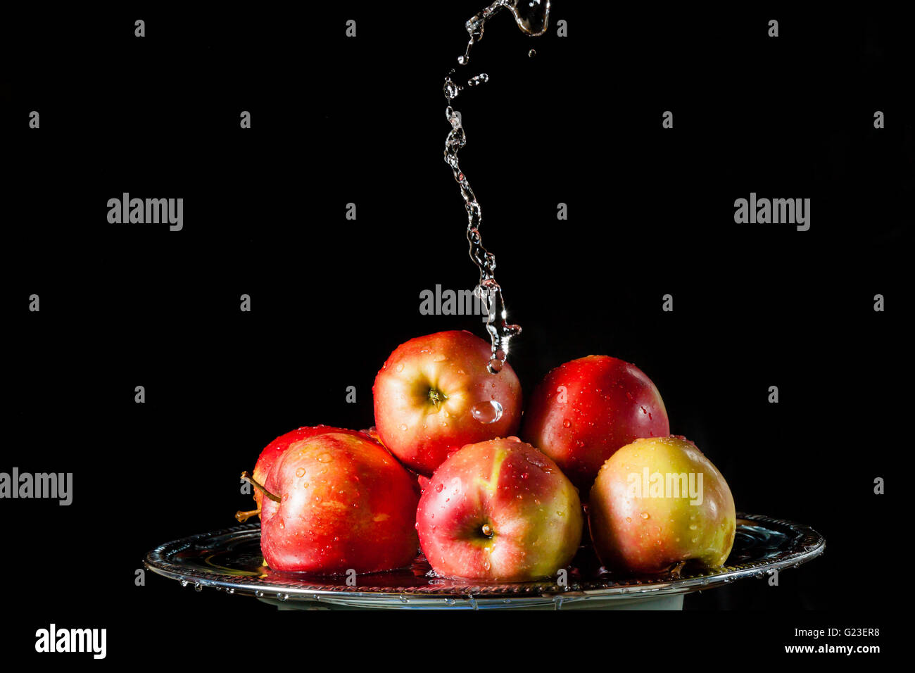 Poche le mele rosse giacente su un silver top e caduta di acqua su sfondo nero Foto Stock