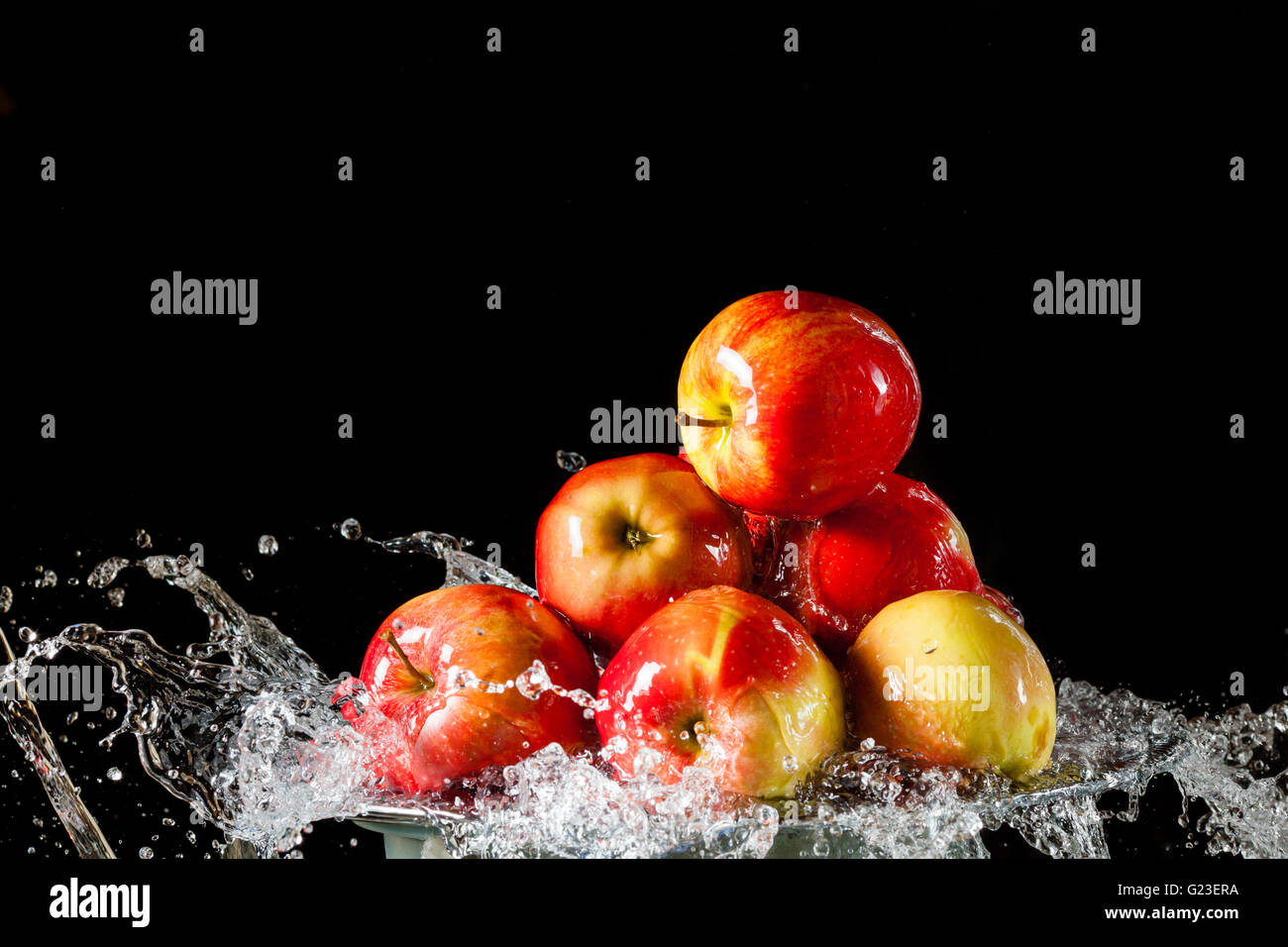 Poche le mele rosse che giace sul lato di argento e battenti di acqua su uno sfondo nero Foto Stock