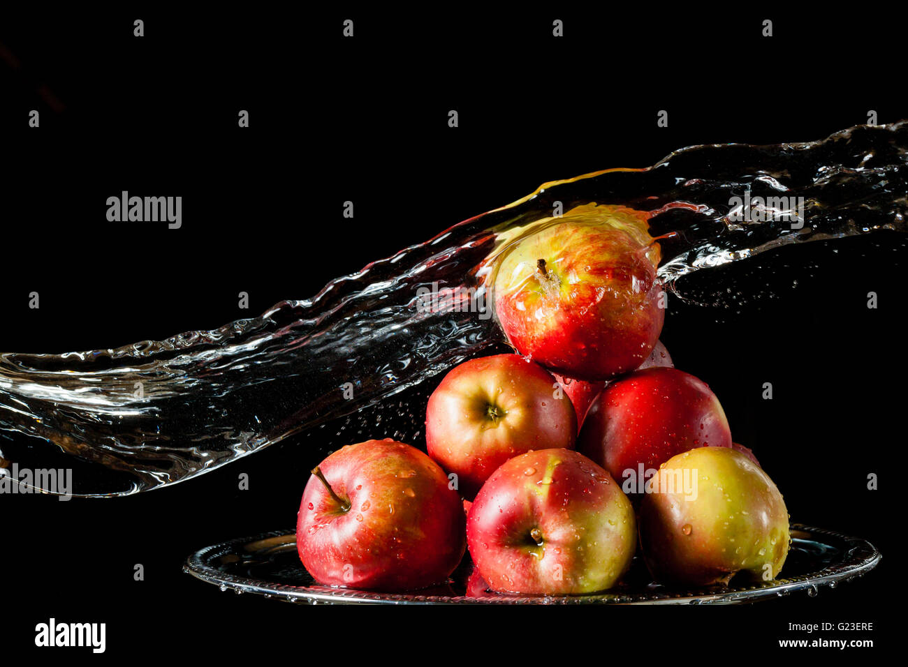 Poche le mele rosse che giace sul lato di argento e battenti di acqua su uno sfondo nero Foto Stock
