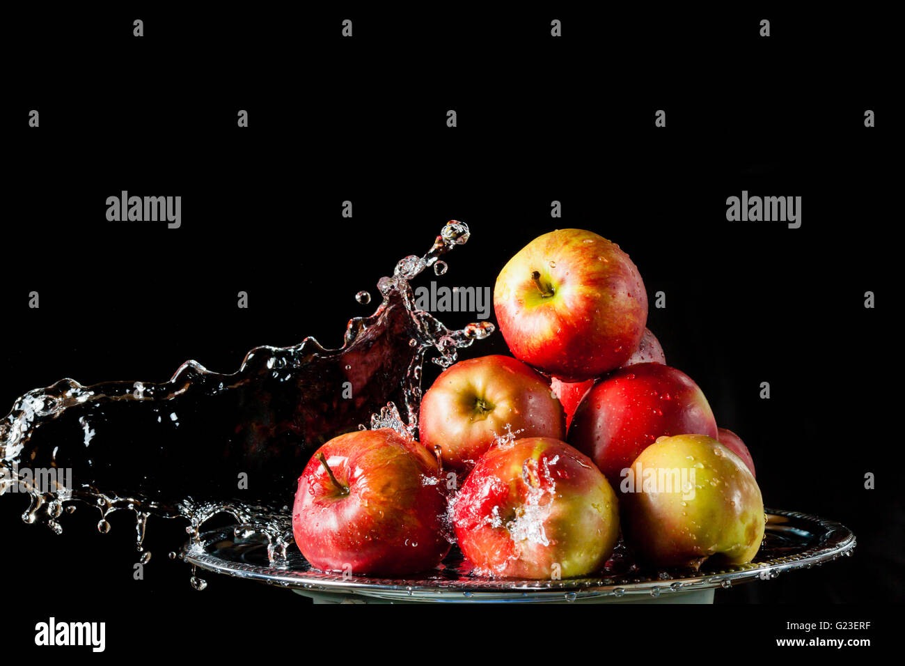 Poche le mele rosse che giace sul lato di argento e battenti di acqua su uno sfondo nero Foto Stock