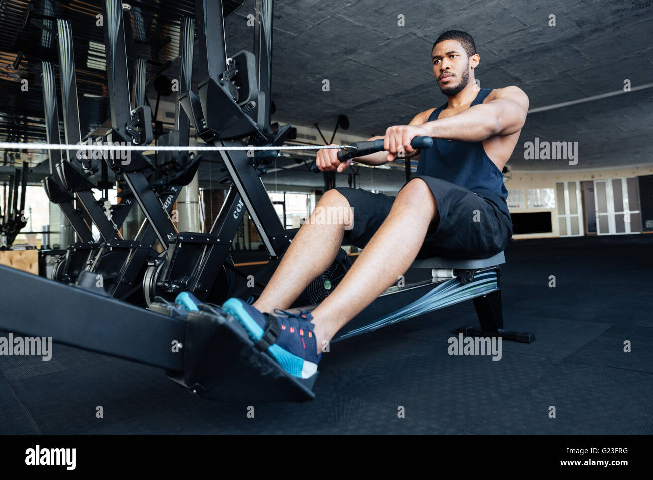 Montare muscolare uomo con vogatore in palestra Foto Stock