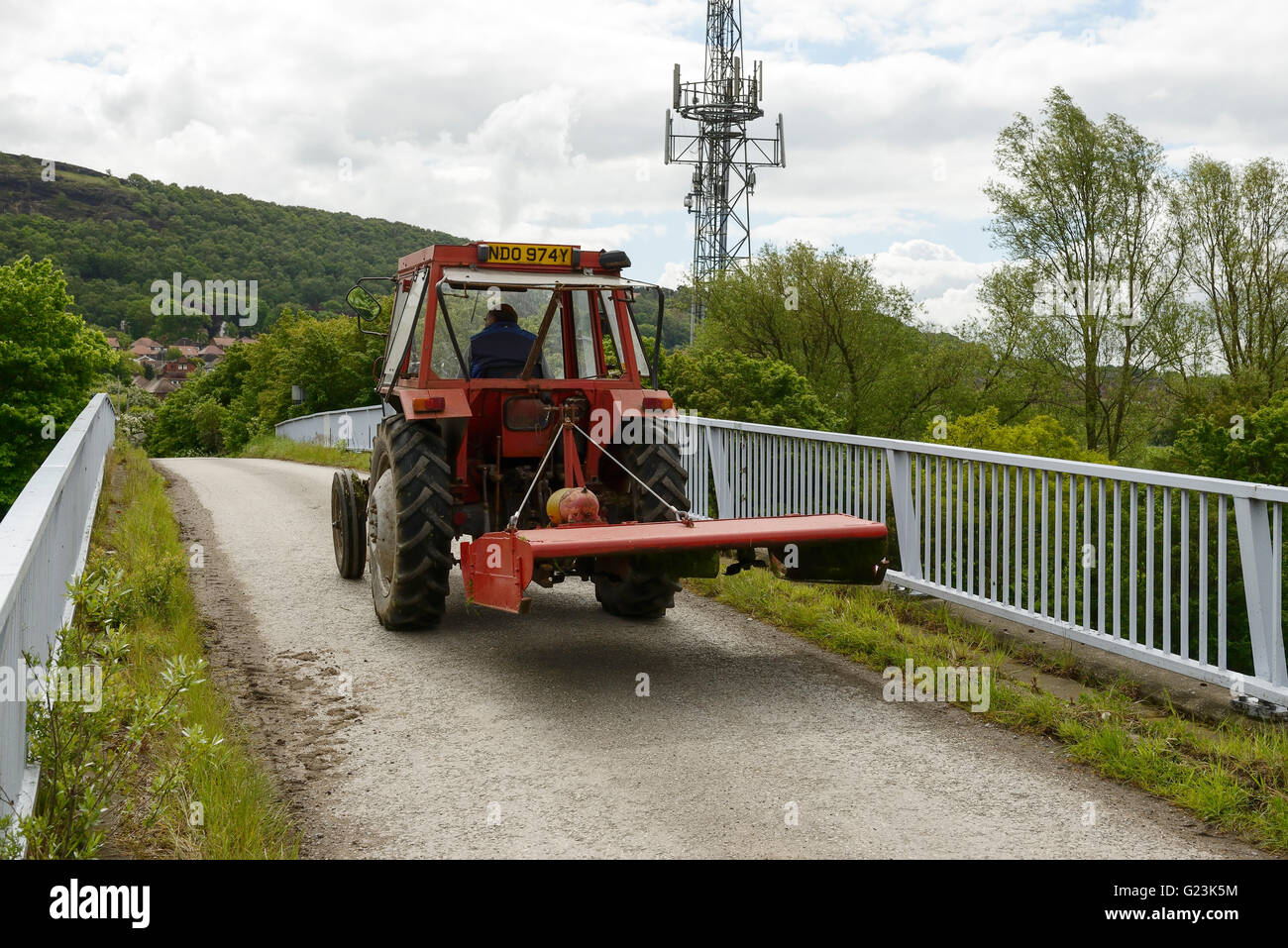 Un agricoltore aziona un trattore lungo una strada che attraversa il M56 Autostrada nel Cheshire Regno Unito Foto Stock