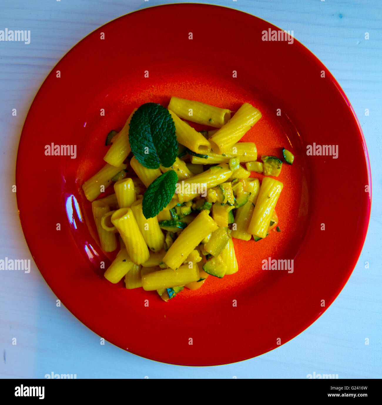 Piatto rosso con pasta condita con fiori di zucca, verdure, zafferano e muentuccia, cibo sano per l'estate Foto Stock