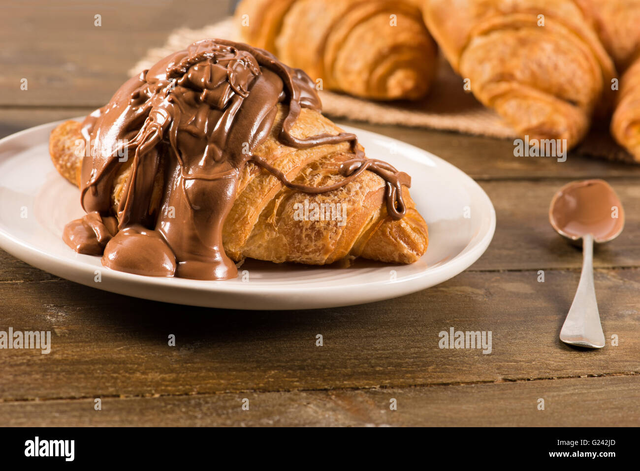 Croissant con cioccolato sulla parte superiore e cucchiaio e altri croissant sullo sfondo Foto Stock