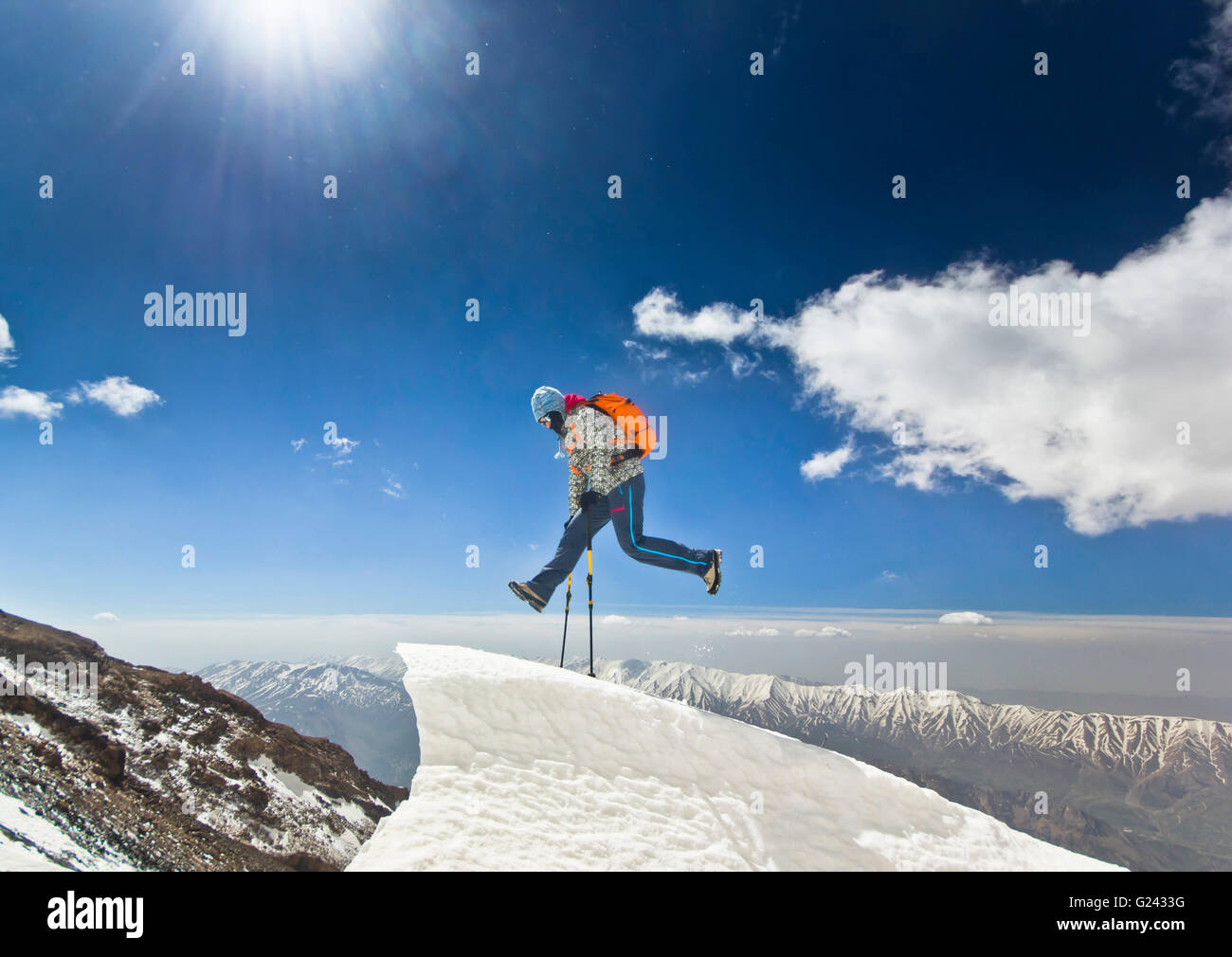 Uomo felice con zaino arancione e due poli jumpingon una scogliera in montagne di sunrise Foto Stock