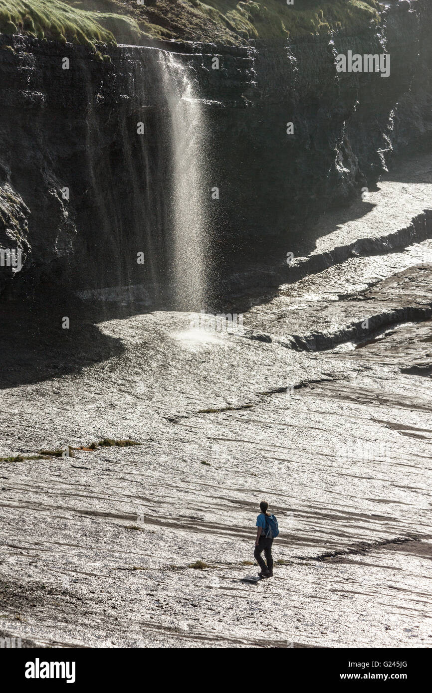 Walker su rocce umide sotto la cascata sulla costa del loop della sezione di testa della costa, County Clare, Irlanda Foto Stock