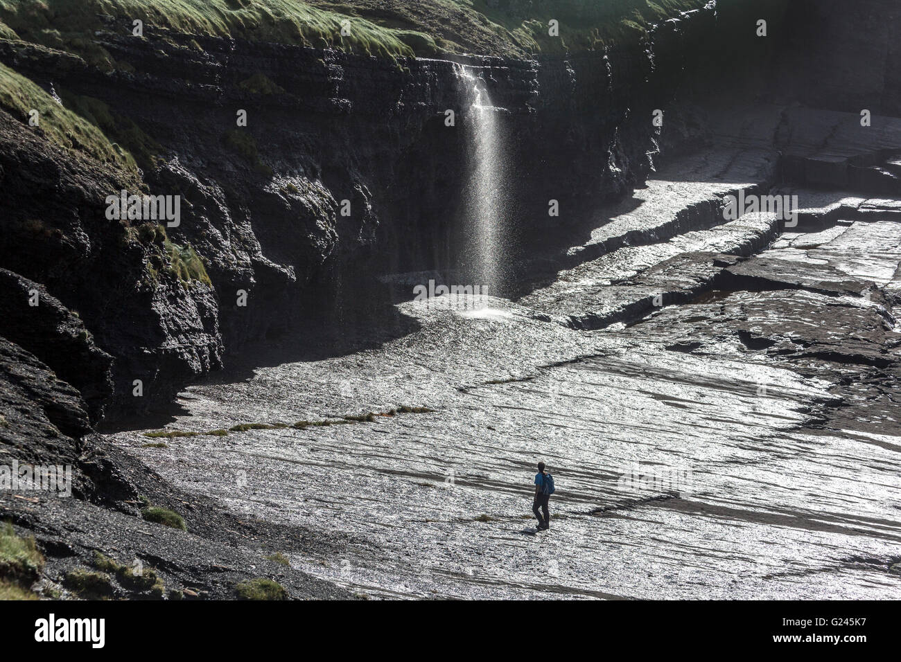Walker su rocce umide sotto la cascata sulla costa del loop della sezione di testa della costa, County Clare, Irlanda Foto Stock
