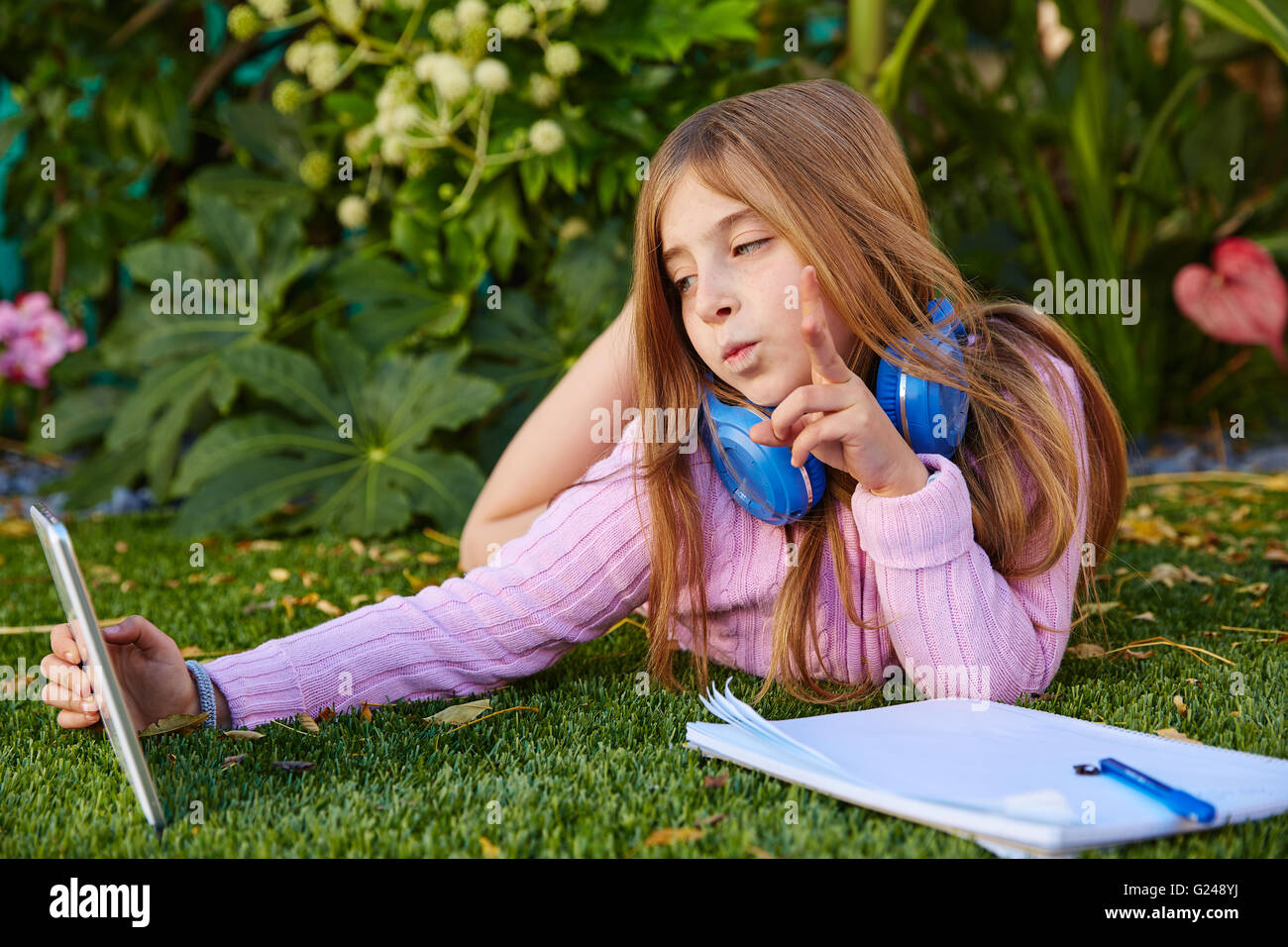 Bionda ragazza di capretto selfie foto con tablet pc giacente sul tappeto erboso di erba con le cuffie Foto Stock