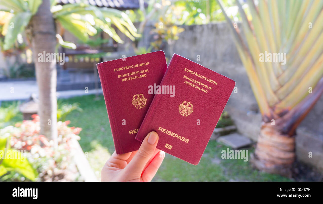 Mano che regge due passaporti tedeschi di fronte a un bel giardino tropicale Foto Stock