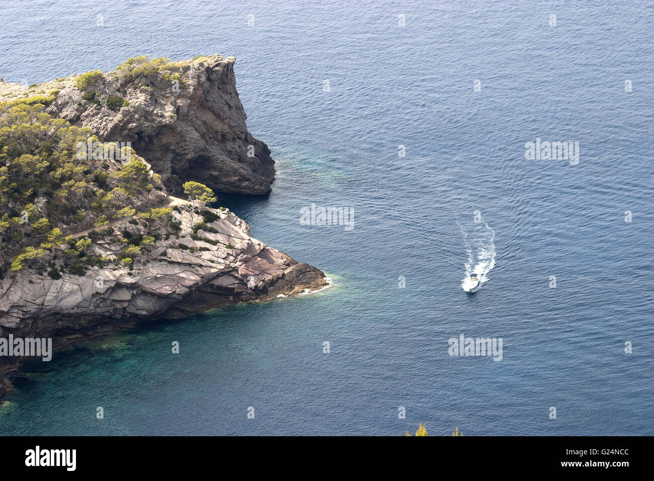 Una bella immagine della costa da una distanza con un piccolo yacht passando per la vegetazione e le rocce in Palma de Mallorca, Spagna Foto Stock