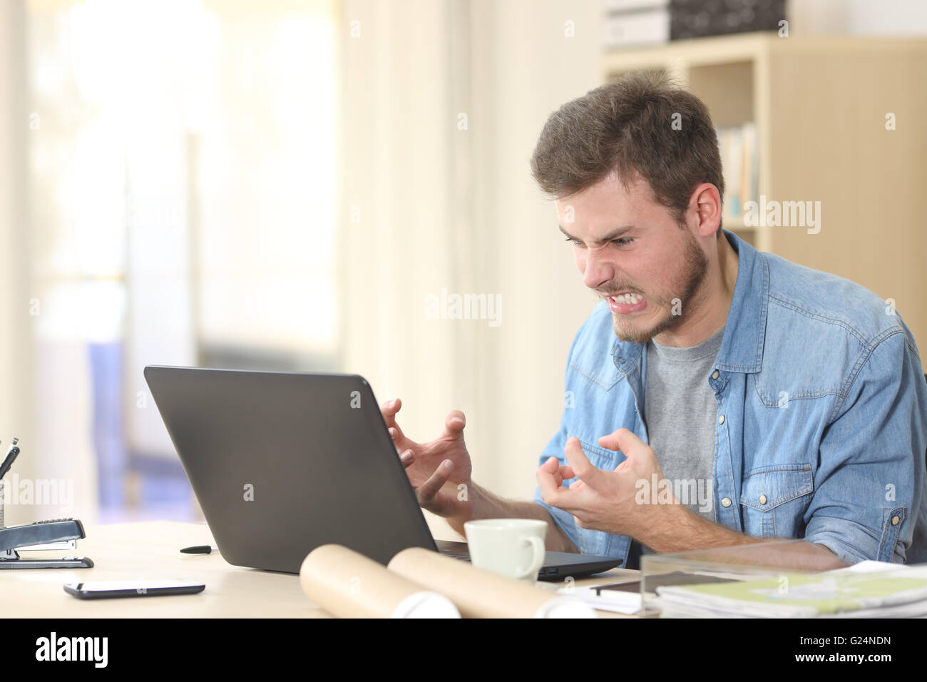 Imprenditore arrabbiato e furioso con un computer portatile in un piccolo ufficio o a casa Foto Stock