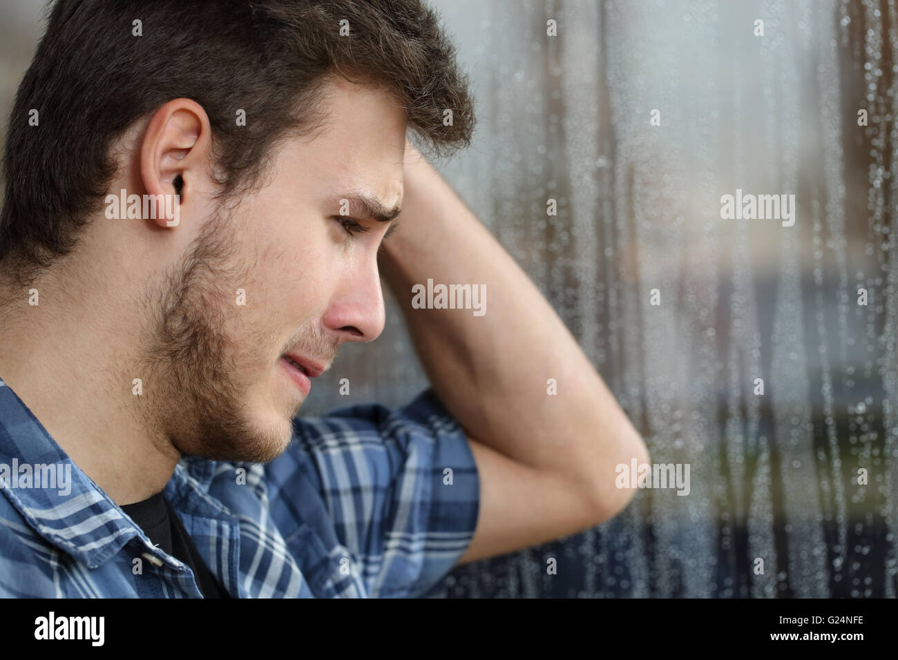 Vista laterale di un uomo triste guardando attraverso la finestrella quasi gridando in un giorno di pioggia Foto Stock