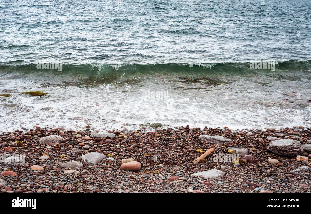 Di ghiaia e di roccia con spiaggia piccola onda in arrivo circa per rompere e acqua schiumosa receding. Foto Stock