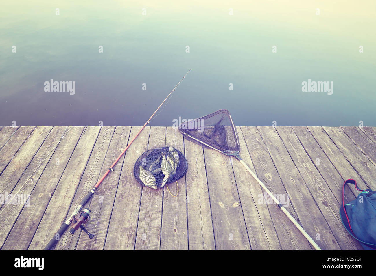 Dai toni rétro di attrezzature da pesca e le catture in rete su un molo in legno. Foto Stock