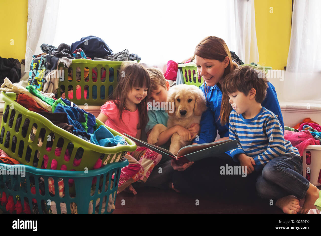 Sorridente lettura madre di tre bambini e golden retriever cucciolo di cane circondato da cesti per la biancheria Foto Stock